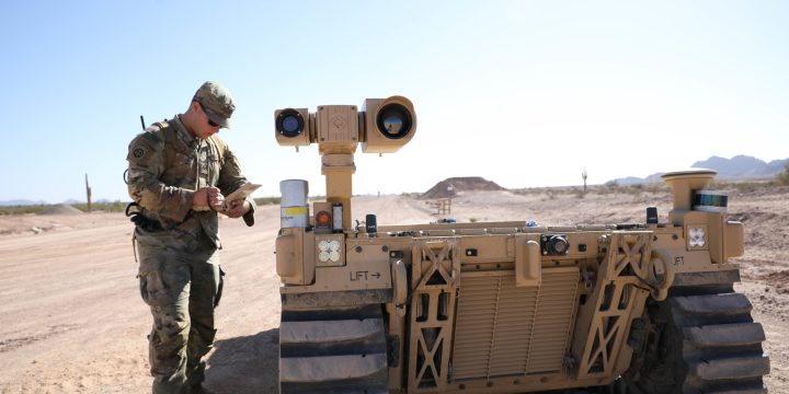 Public domain U.S. Army photo of a soldier using a controller beside an autonomous ground vehicle at a desert test range