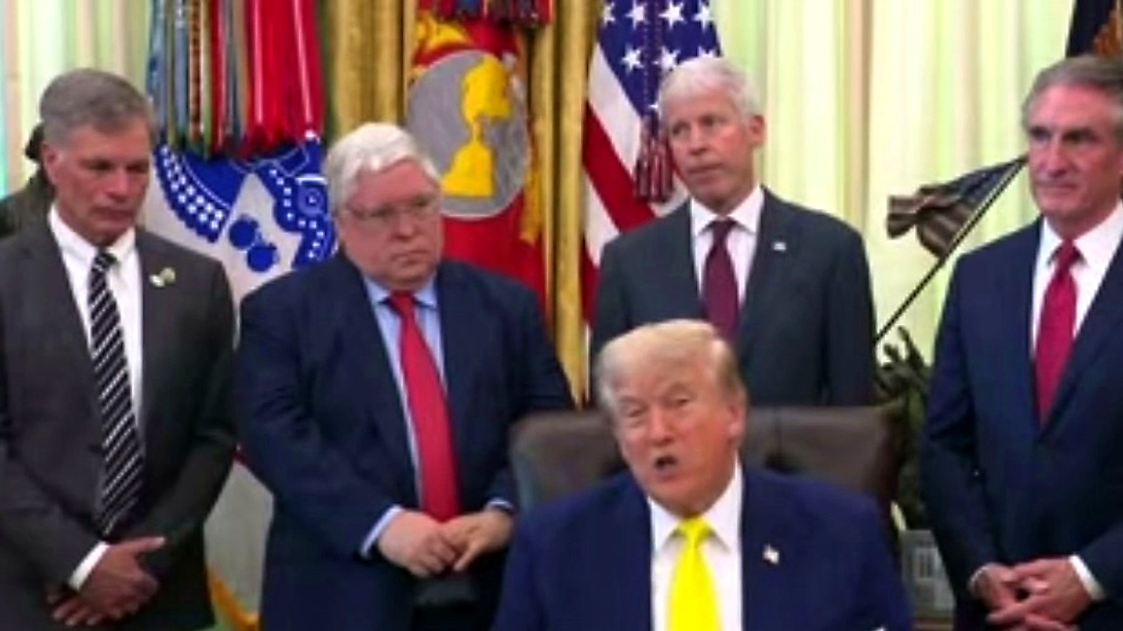 President Trump speaking in the Oval Office with officials behind him