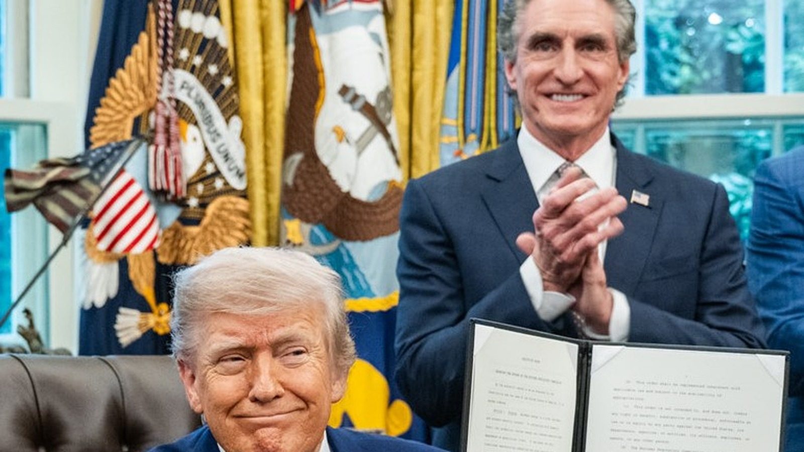 President Trump seated at the Oval Office desk with Secretary Doug Burgum standing behind him