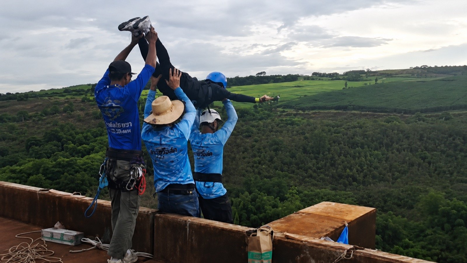 Operators position a person for a rope jump over a green valley