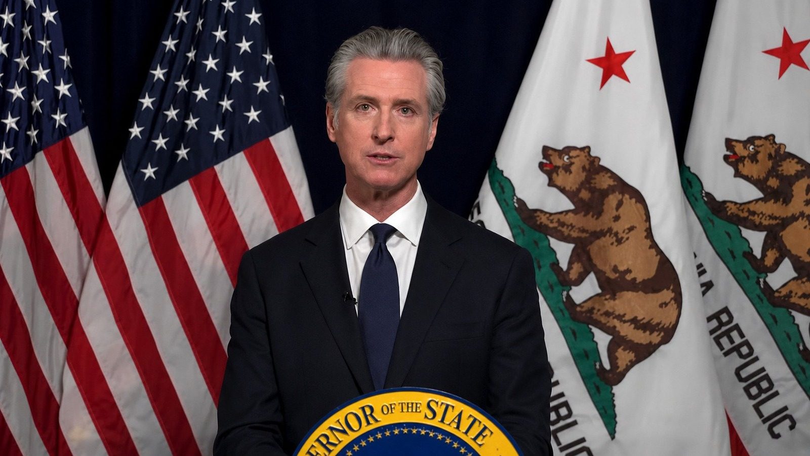 California Governor Gavin Newsom speaks at a podium with U.S. and California flags behind him