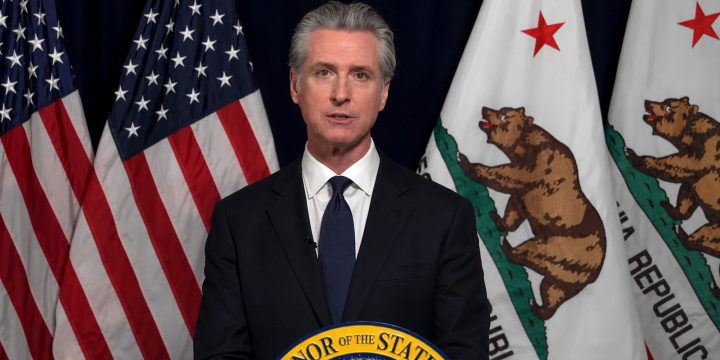 California Governor Gavin Newsom speaks at a podium with U.S. and California flags behind him