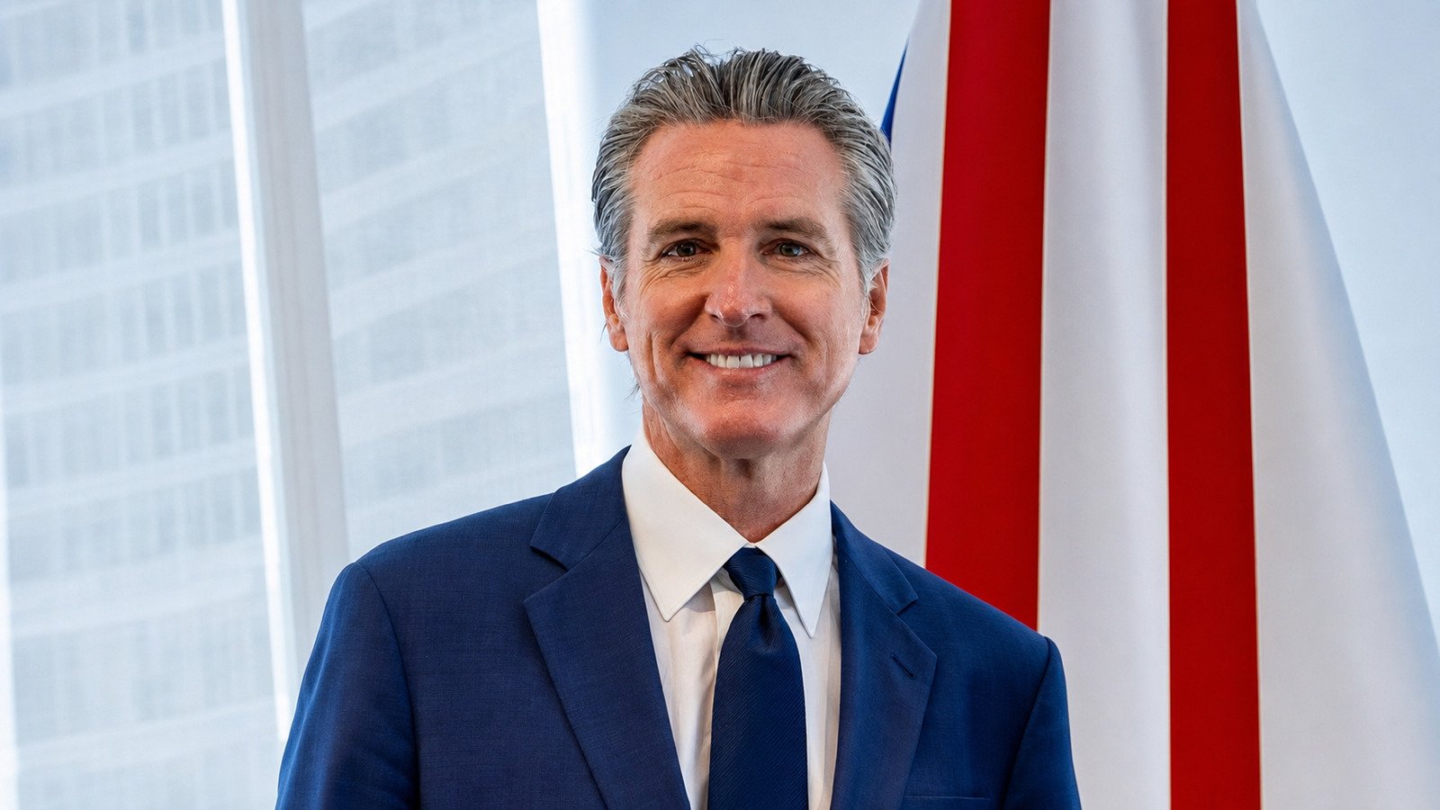 California Governor Gavin Newsom in a blue suit beside an American flag