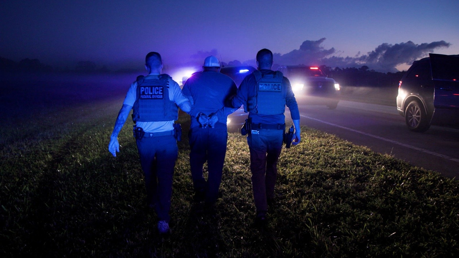 Official U.S. government photo of federal ICE officers escorting a handcuffed man beside law enforcement vehicles during a targeted operation
