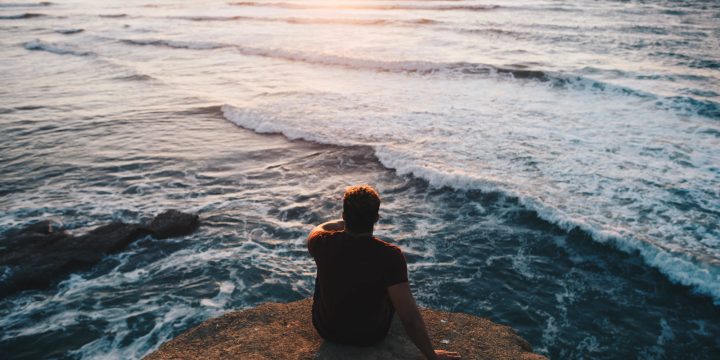 A visitor sits on a rocky ledge above Pacific waves at Sunset Cliffs in San Diego